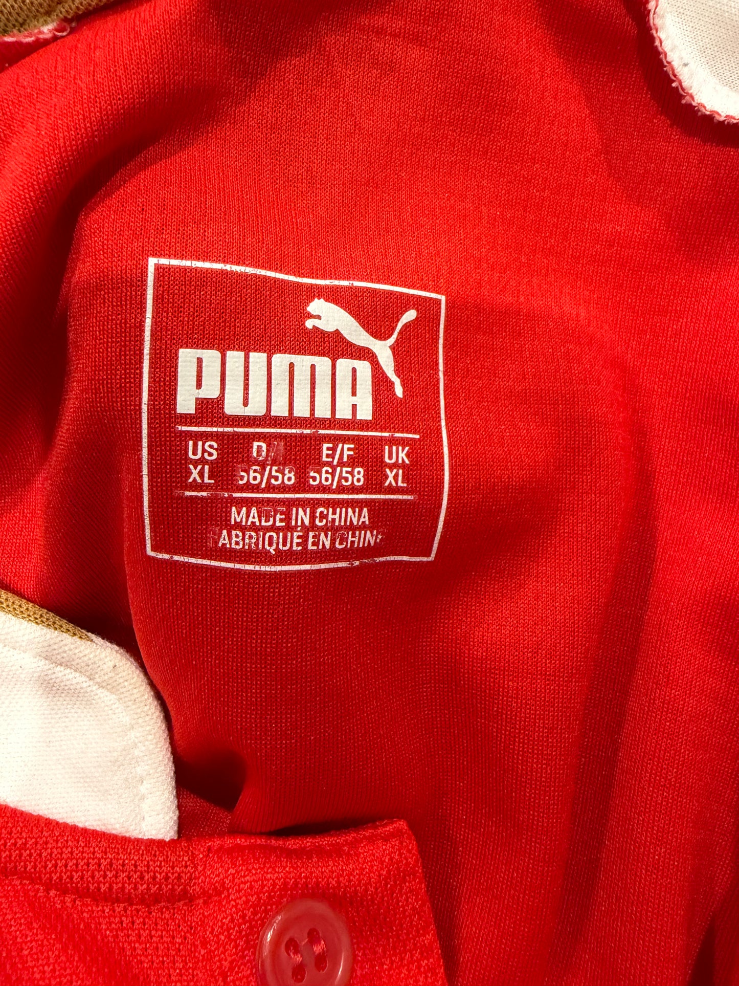 Close-up of a red Puma garment showing the white Puma logo and size label patch on the chest.