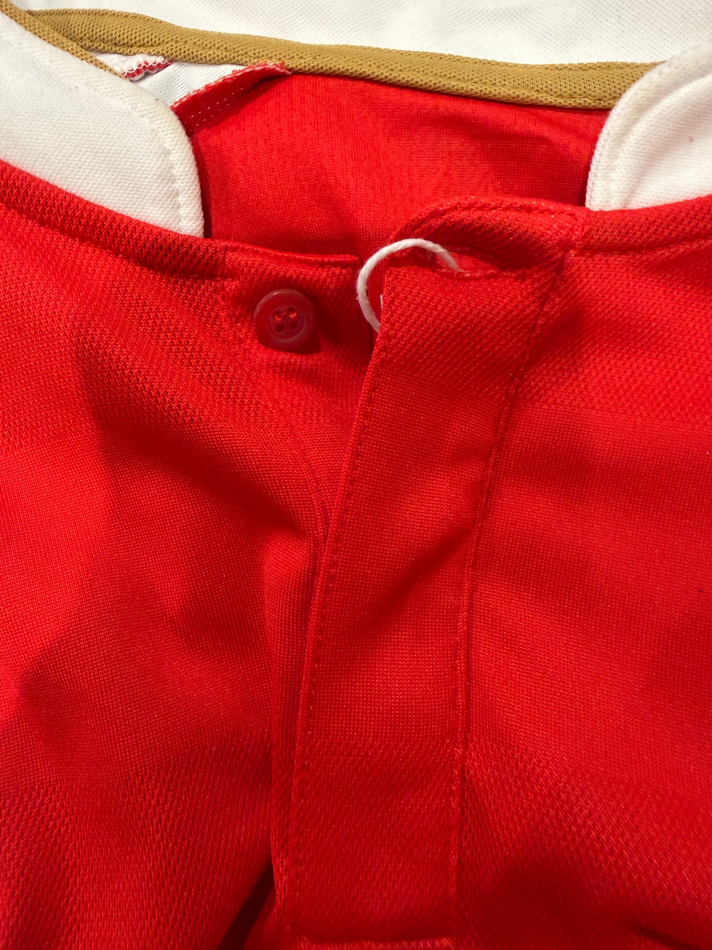 Close-up of a red textured fabric garment, showing a button closure, white drawstring loop, and white inner lining.