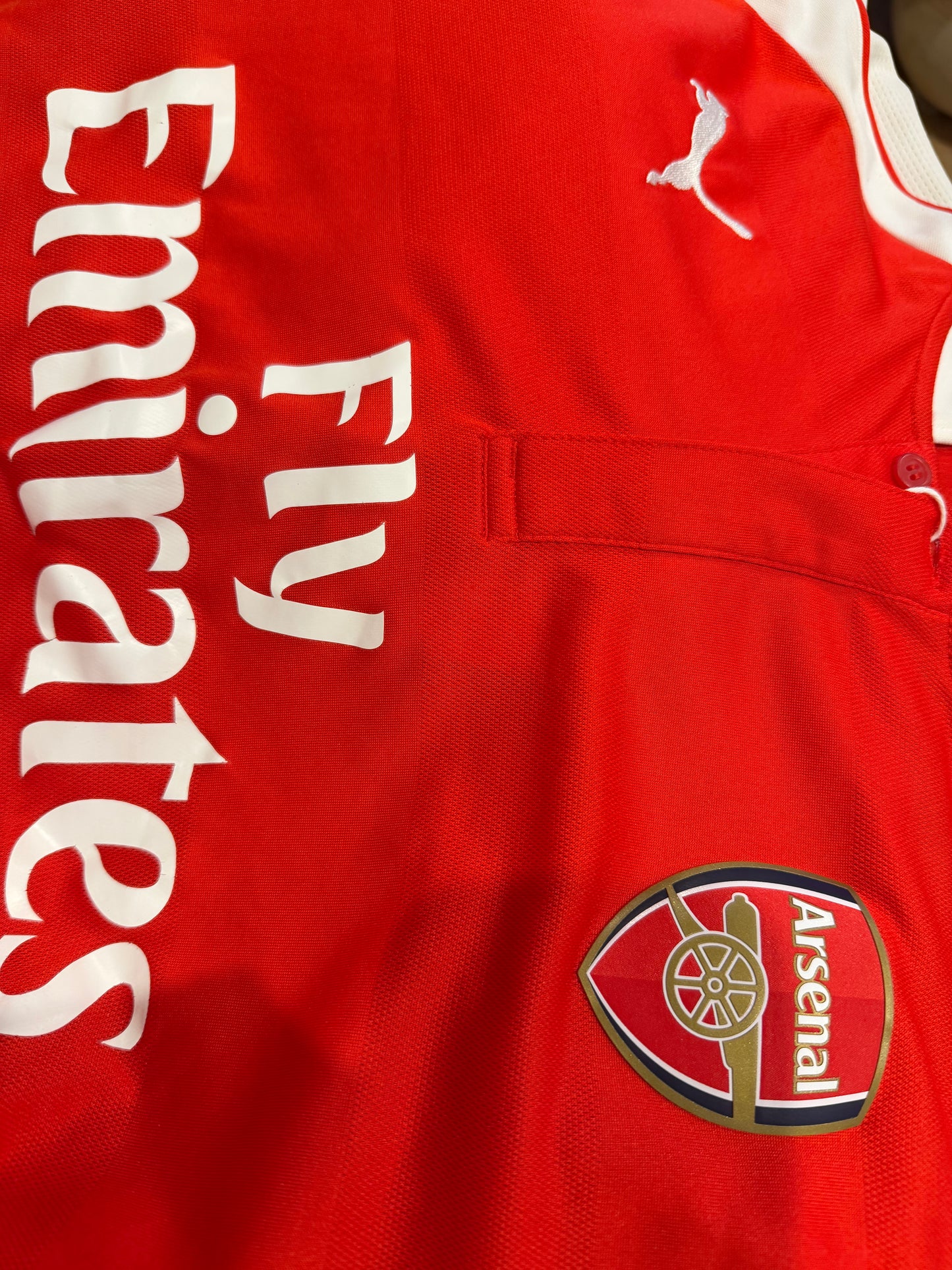 Close-up of a red Arsenal soccer jersey showing the Fly Emirates sponsor logo, the Puma logo, and the Arsenal club crest.