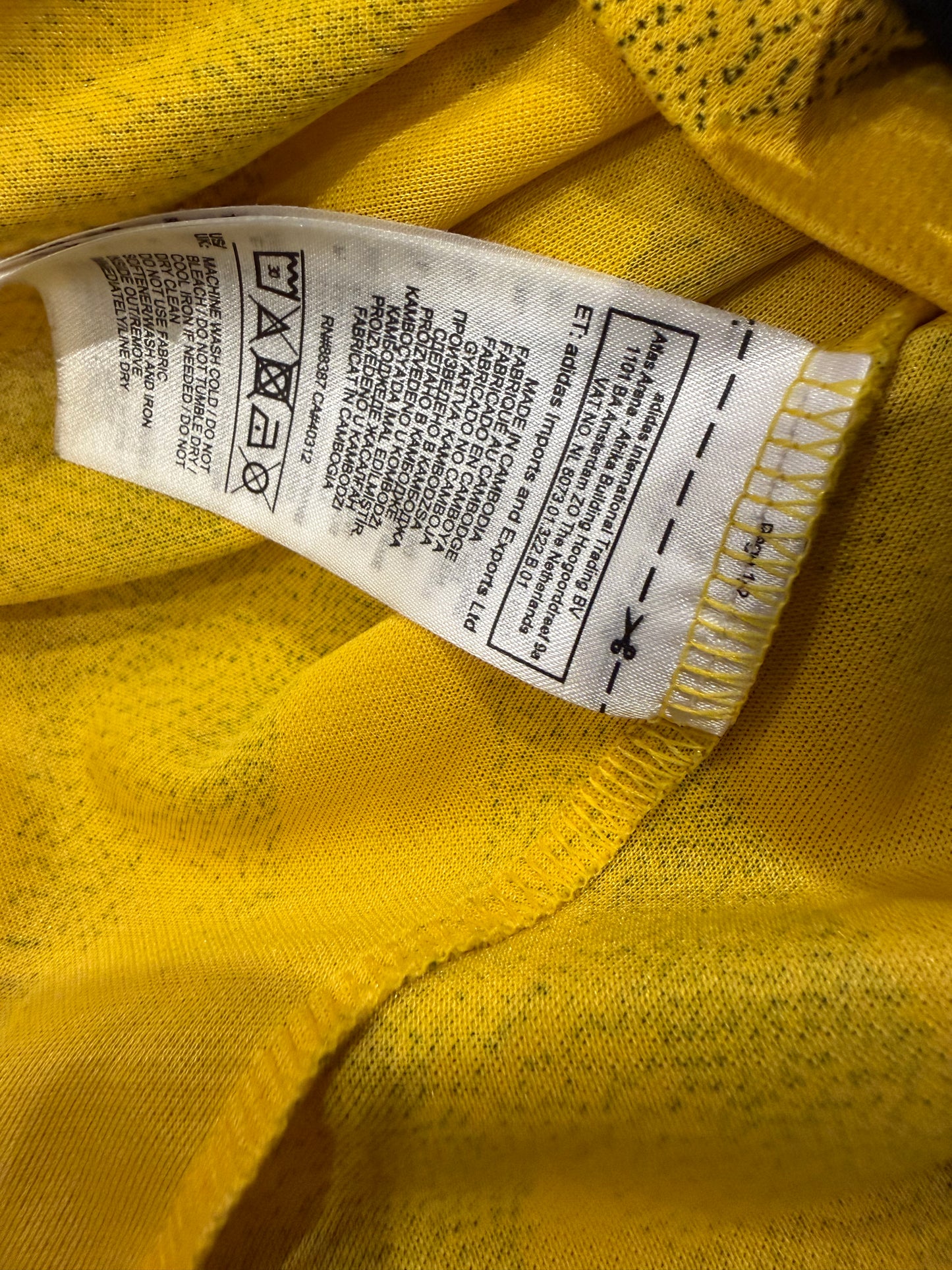 Close-up of a yellow knit garment showing the interior neck label with care instructions and size information.