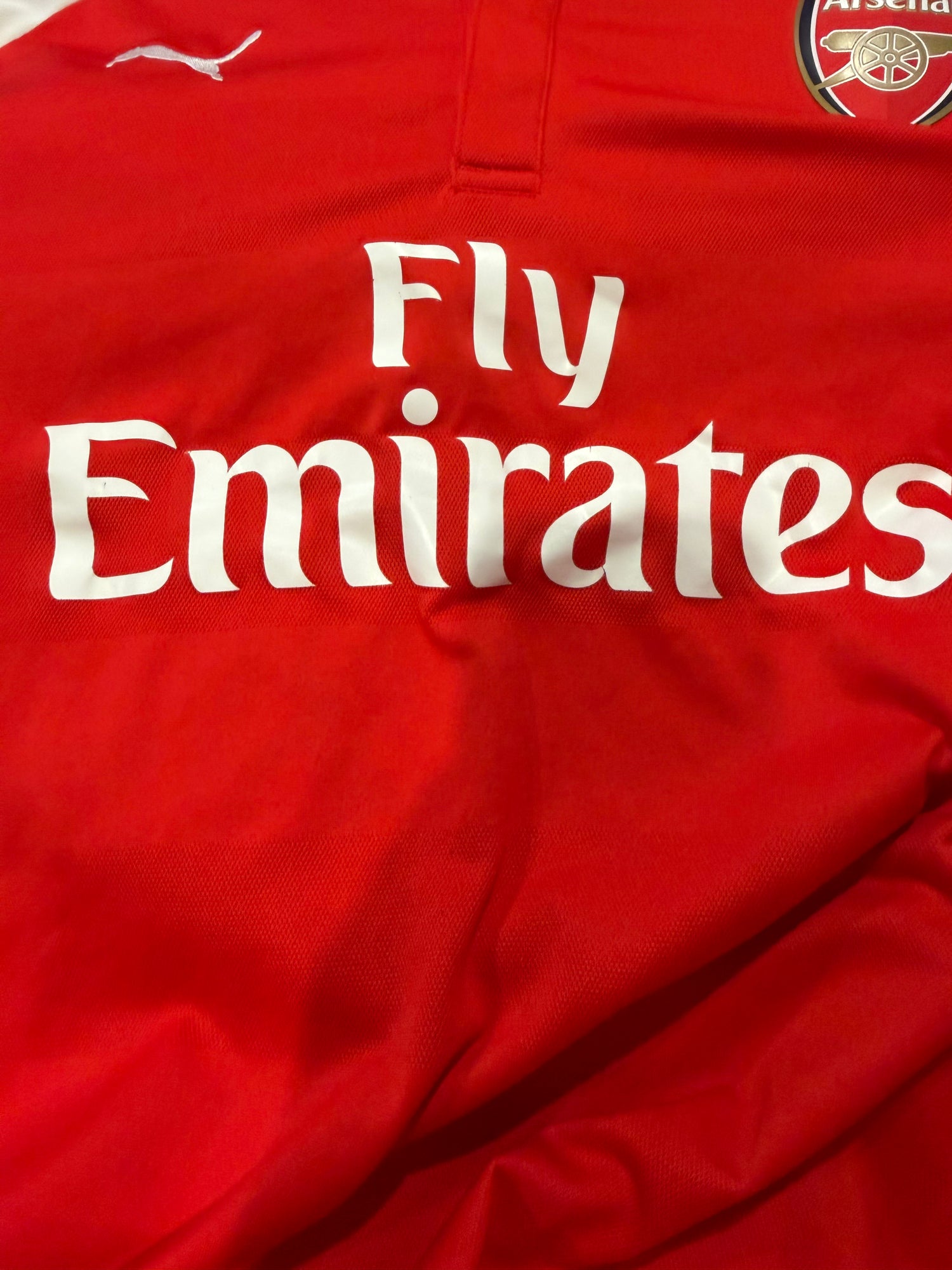Close-up of a red Arsenal soccer jersey with the white Puma logo, Arsenal crest, and large white Fly Emirates sponsor text.