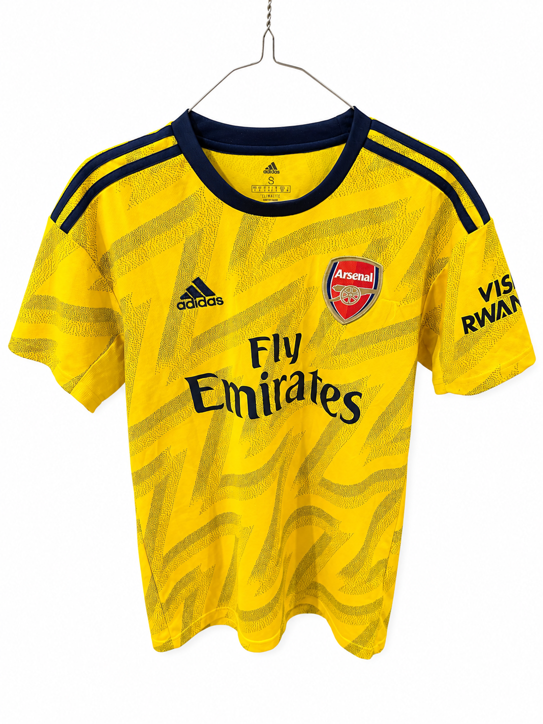 A yellow Arsenal home soccer jersey by Adidas, featuring a subtle wavy pattern, hanging on a metal hanger against a white background. The jersey includes the Arsenal club crest, the Adidas logo, and the Fly Emirates sponsor logo.