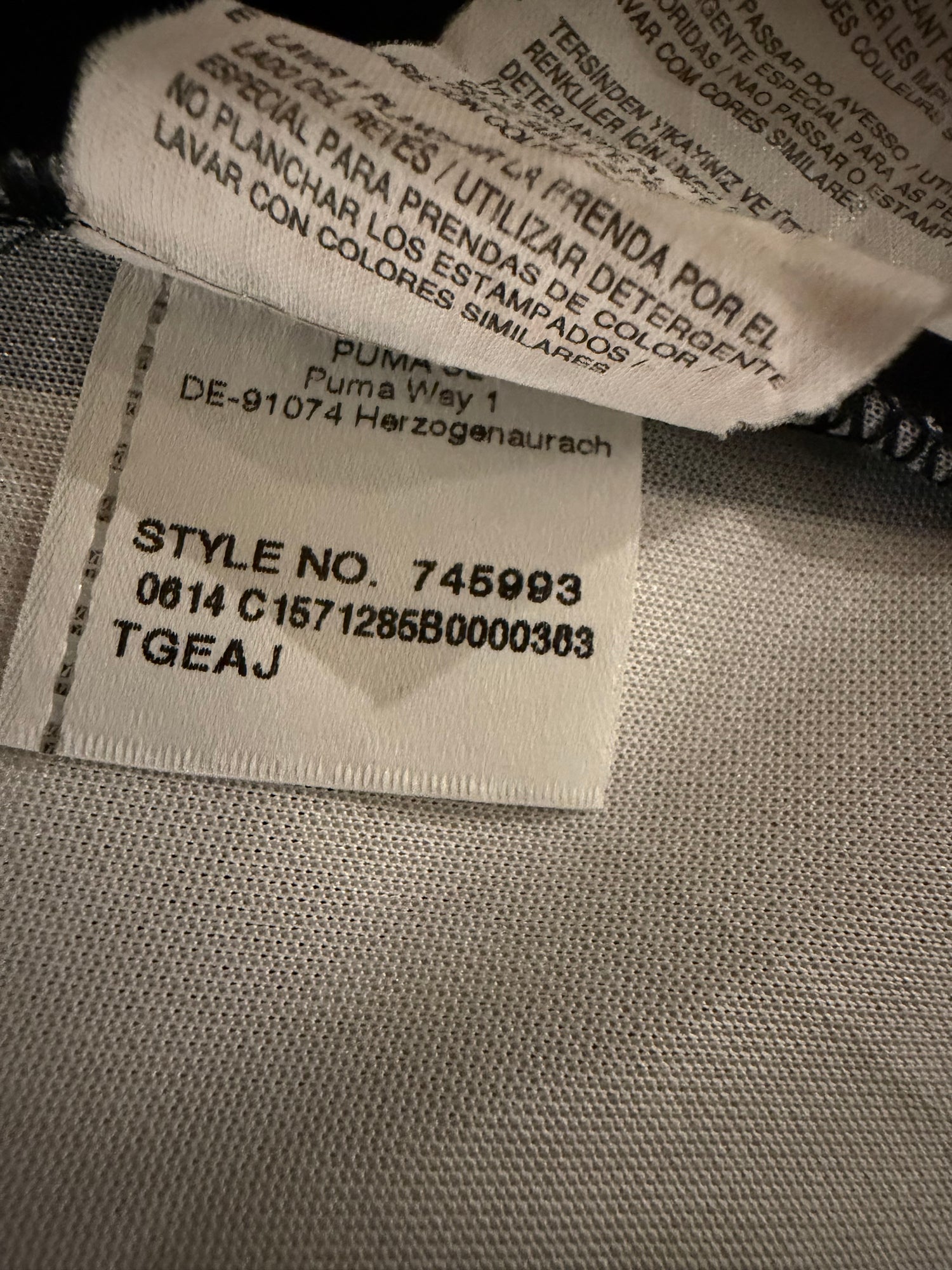 Close-up of a garment's interior label showing text including 'PUMA' and 'Style No. 745993' on a light gray woven fabric background.